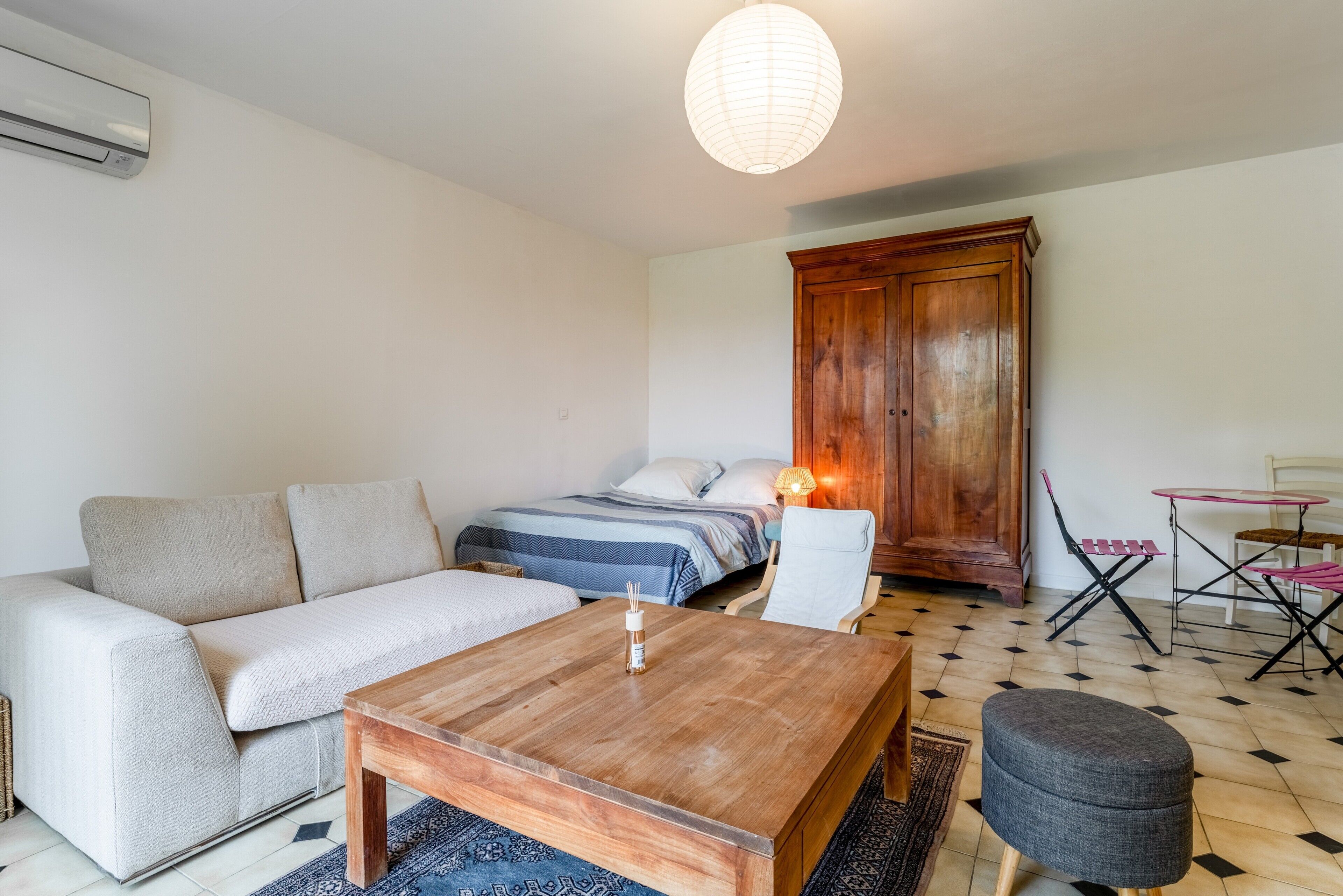 Une pièce comprenant un canapé, une table basse en bois, un lit avec une couverture bleue, une armoire, une petite table avec une lampe et un tapis à motifs.