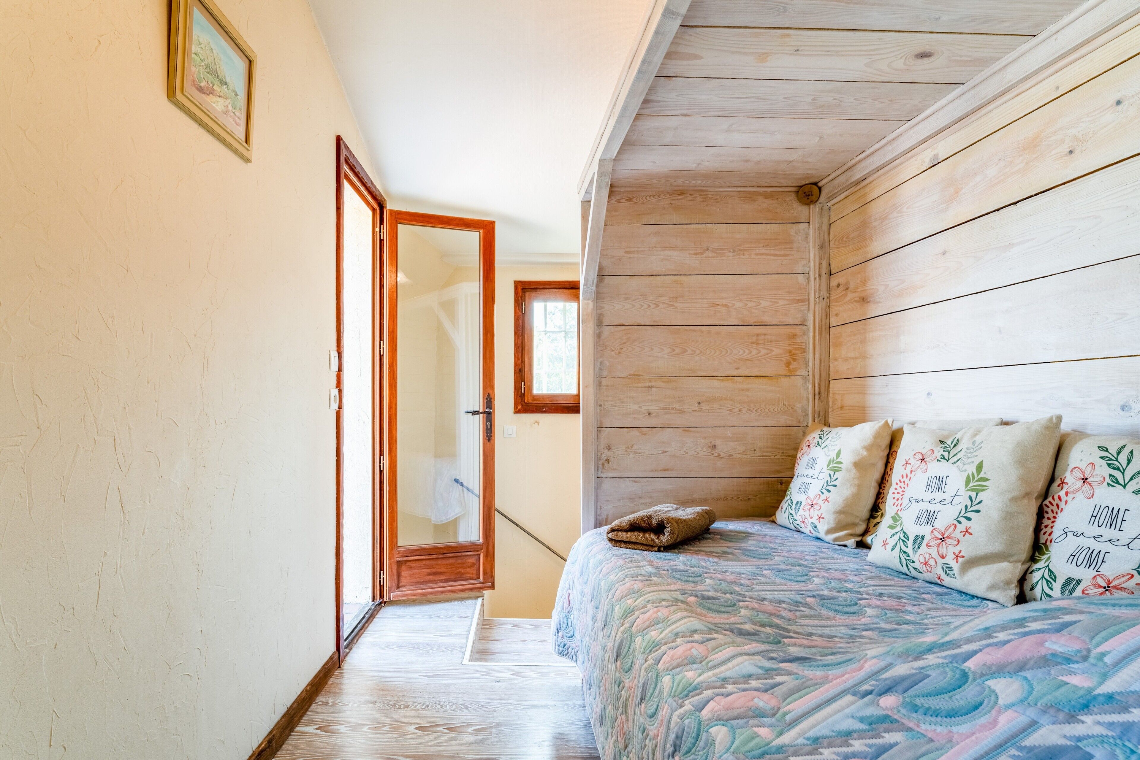 A bedroom with a wooden ceiling, a bed with floral pillows, and a door leading to a bathroom.