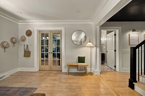 Een gang met houten vloer, een bank, een spiegel en een deur naar een andere kamer.