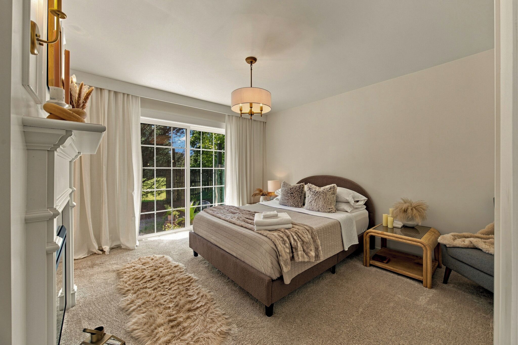 A bedroom with a large bed, a nightstand, a lamp, a chair, and a view of the outdoors through a sliding door.