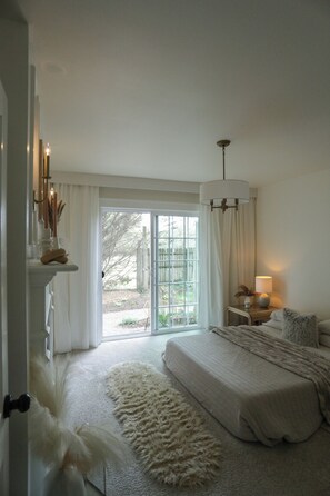 Quarto com uma cama grande, uma mesa de cabeceira com abajur, um tapete fofinho e vista para o exterior através de uma porta de correr de vidro.