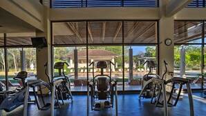 Une salle de sport équipée de machines de cardio et offrant une vue sur un bâtiment à l’extérieur.