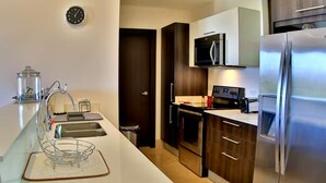Une cuisine moderne équipée d’un réfrigérateur en acier inoxydable, d’un four à micro-ondes et d’une cuisinière. On y trouve un plan de travail blanc avec un évier et une étagère en métal.