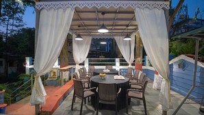 Un espace de restauration en plein air avec une table ronde et des chaises, protégé par un auvent agrémenté de rideaux blancs.