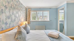 A bedroom with a bed, pillows, a window, and a radiator. - Homely 4 Bedroom House Addlestone (Addlestone)