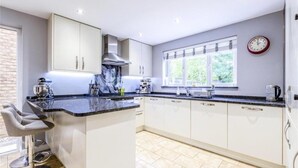 A modern kitchen with white cabinets, a marble countertop, and a built-in island. - Homely 4 Bedroom House Addlestone (Addlestone)