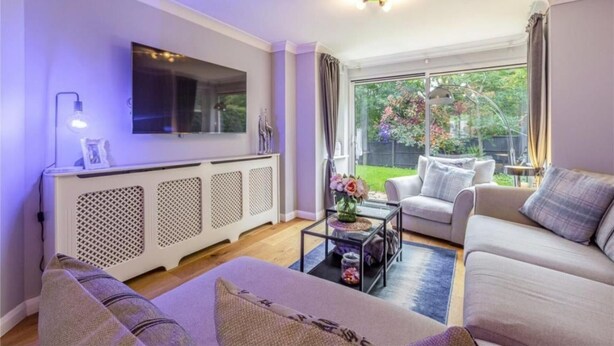 A living room with a sofa, coffee table, and a TV mounted on the wall. - Homely 4 Bedroom House Addlestone (Addlestone)