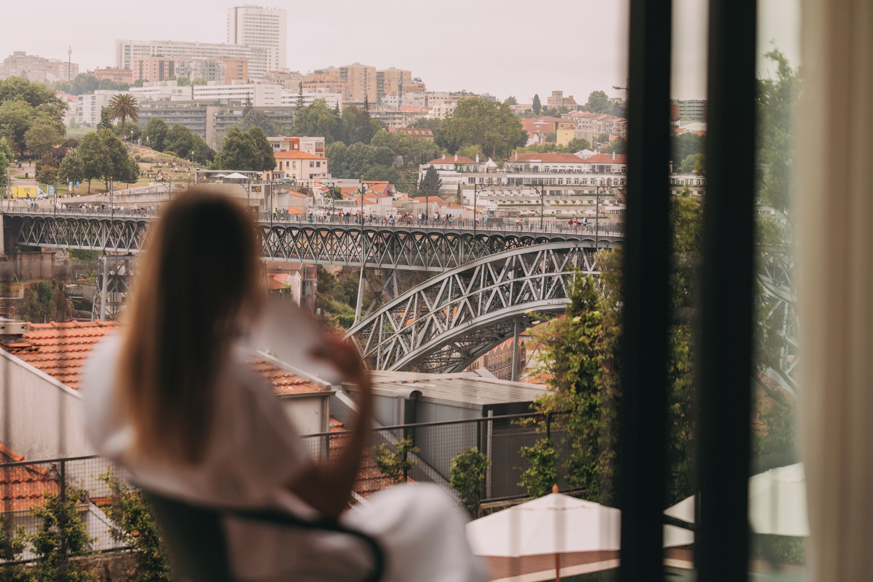 Una persona sentada junto a una ventana con vistas a un paisaje urbano que incluye un puente y edificios.