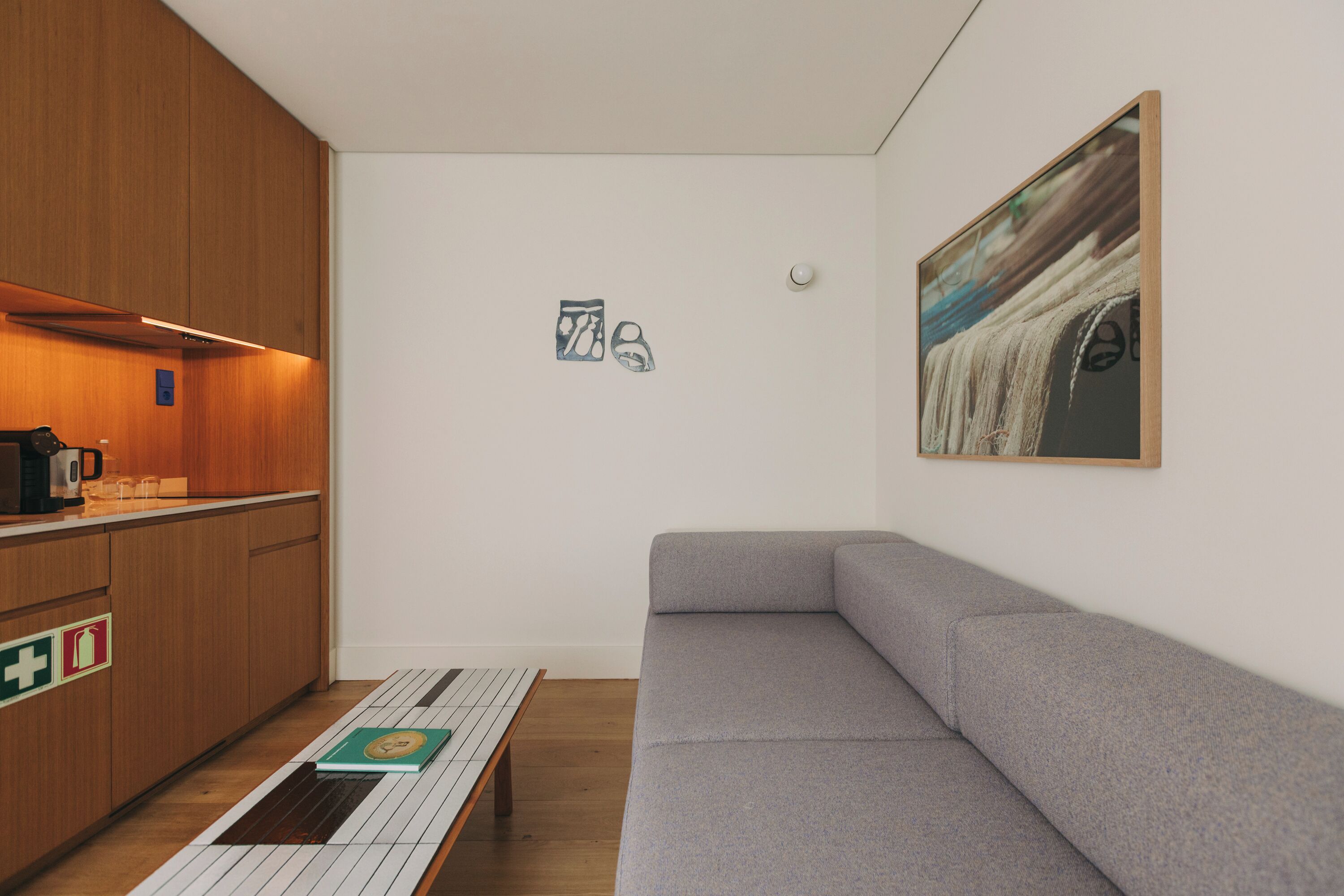 Una habitación moderna con sofá gris, armarios de madera, suelo de baldosas, una mesita y un cuadro colgado en la pared.
