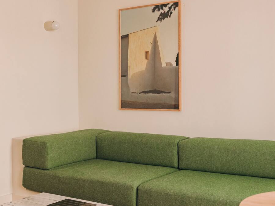 A green sofa against a white wall with a framed picture above it.