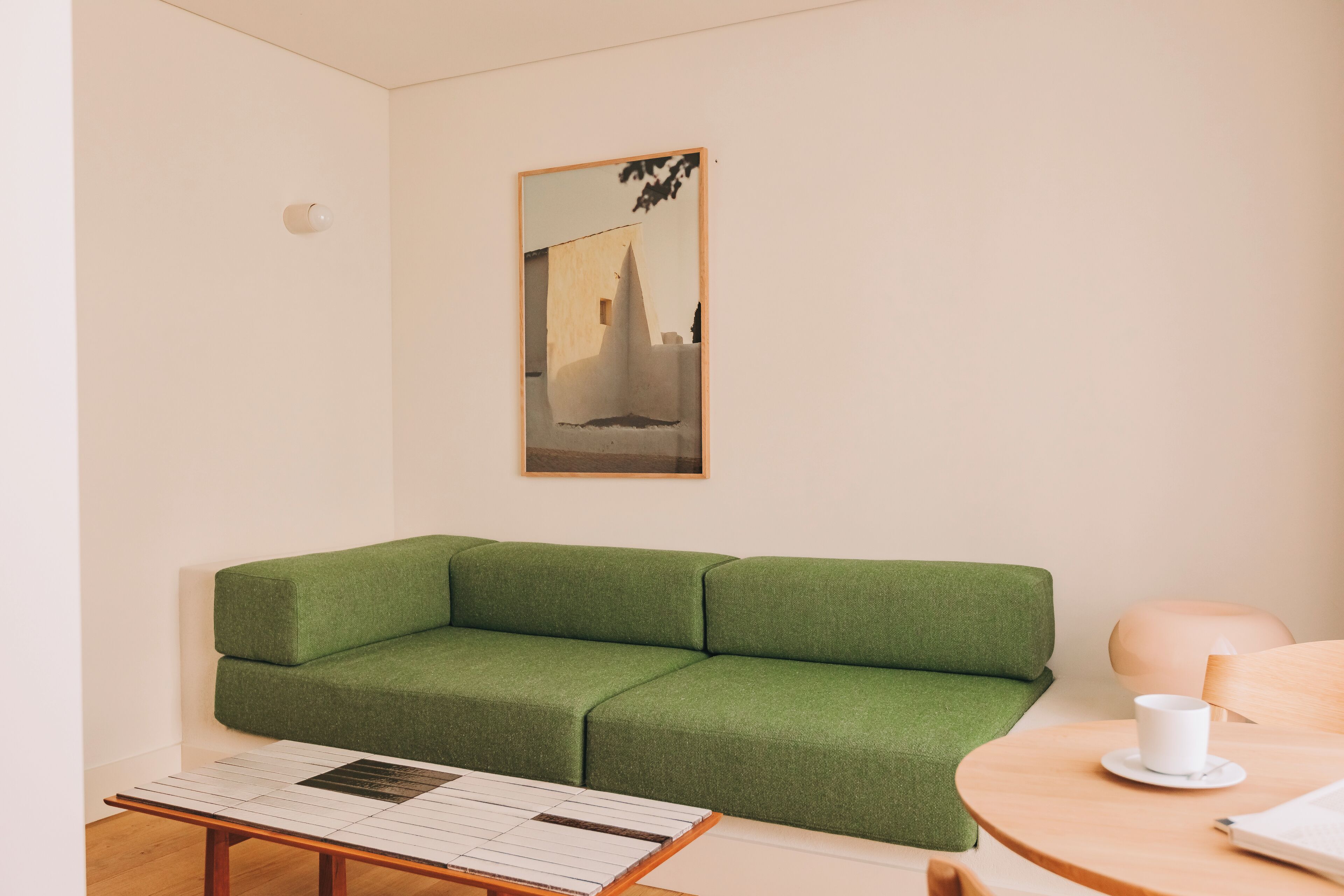 A green sofa, a small table with a white mug, and a framed picture on the wall.