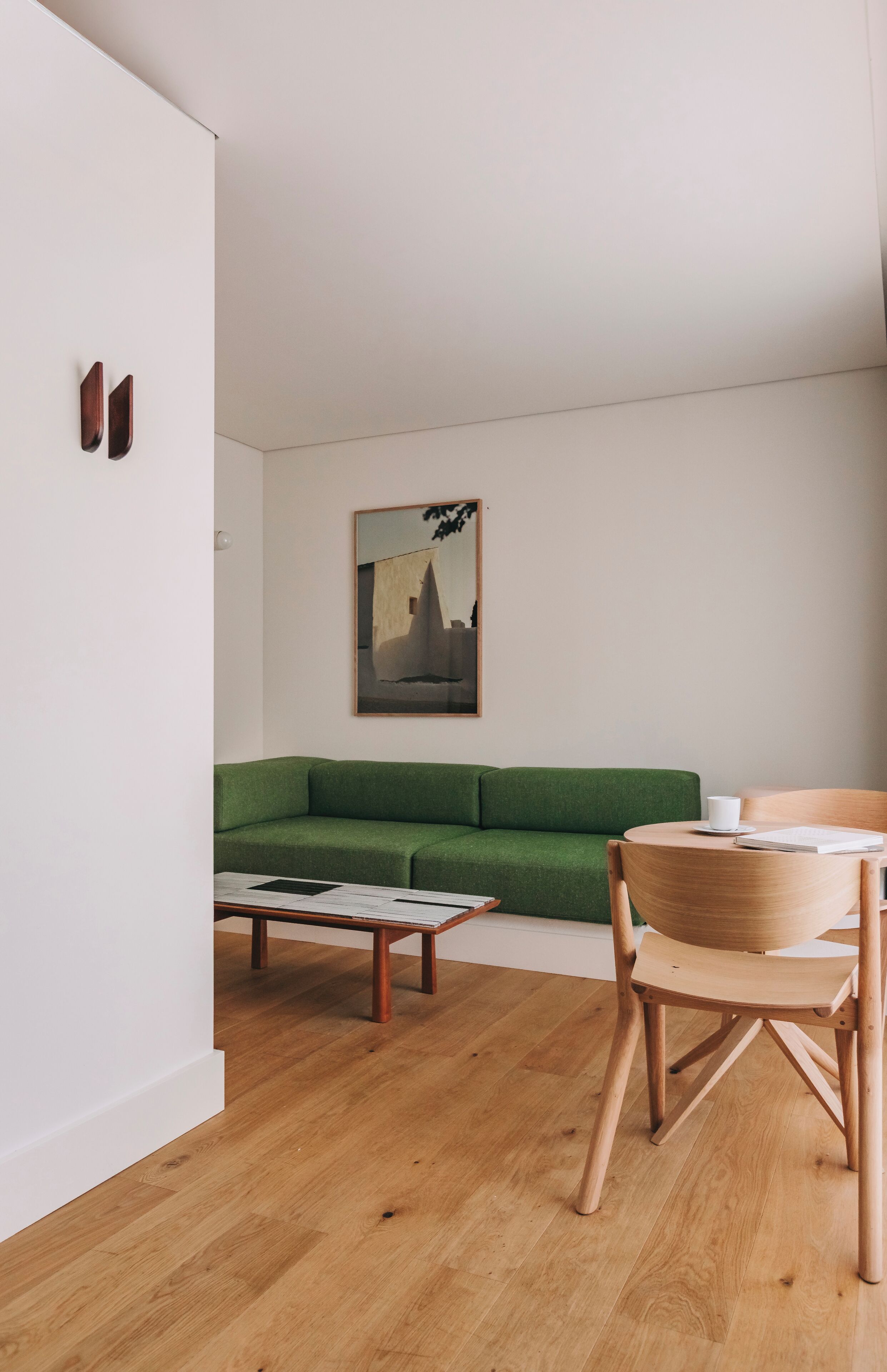 Ein minimalistisches Wohnzimmer mit einem grünen Sofa, einem Holztisch und einem Holzstuhl.
