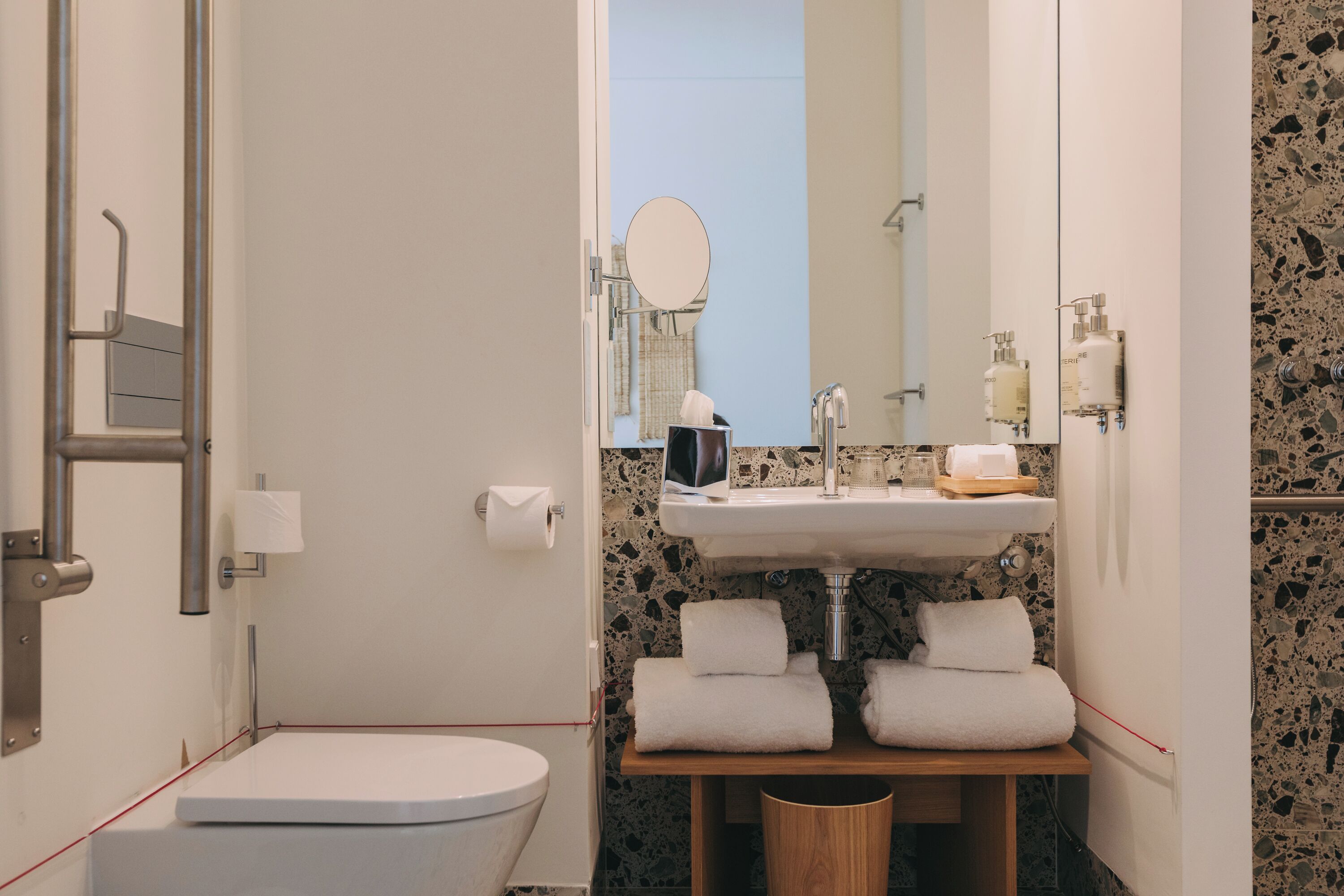 A bathroom with a toilet, sink, mirror, towel rack, and a trash bin.