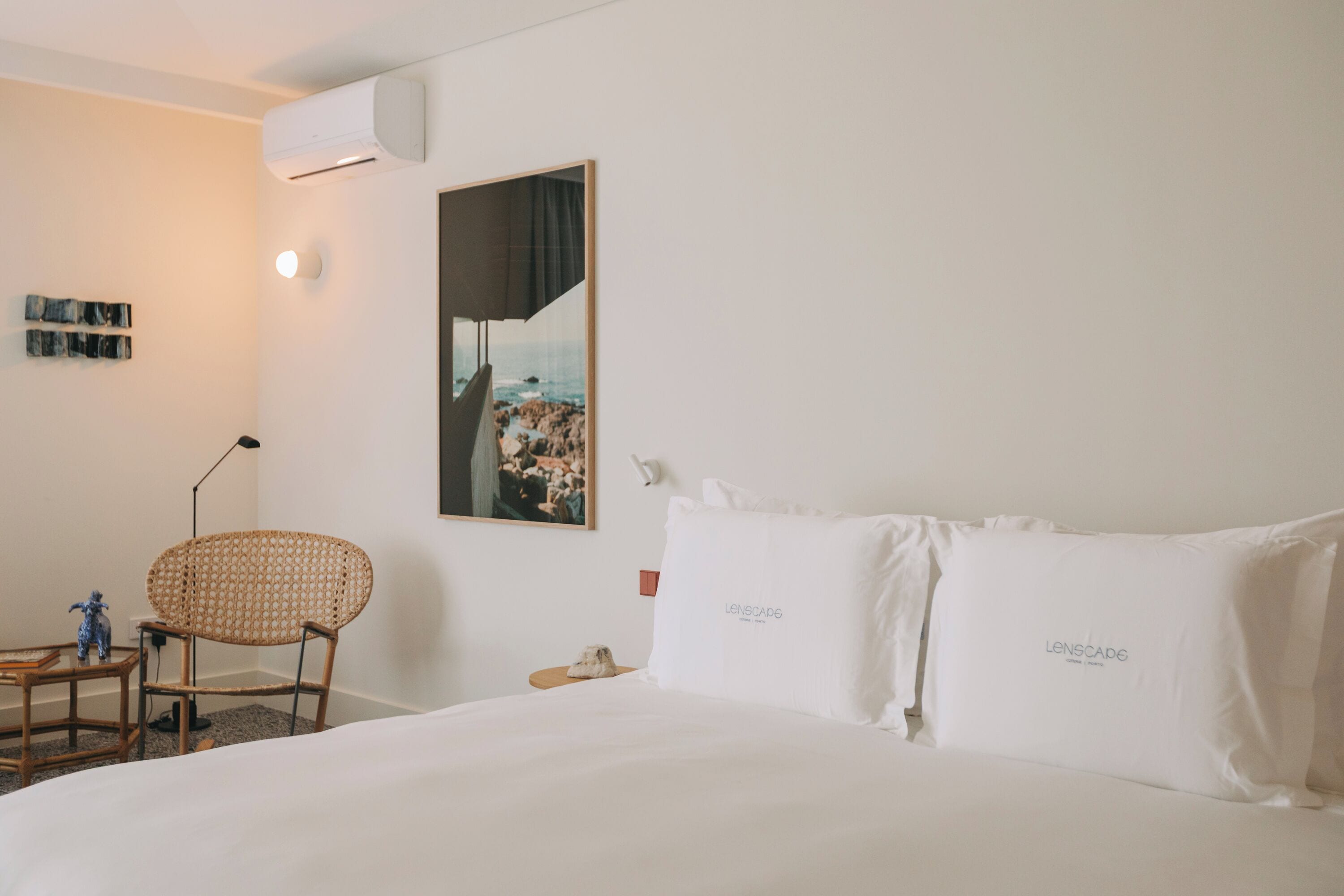 A hotel room with a bed, a chair, a nightstand, a wall-mounted air conditioner, and a framed picture.