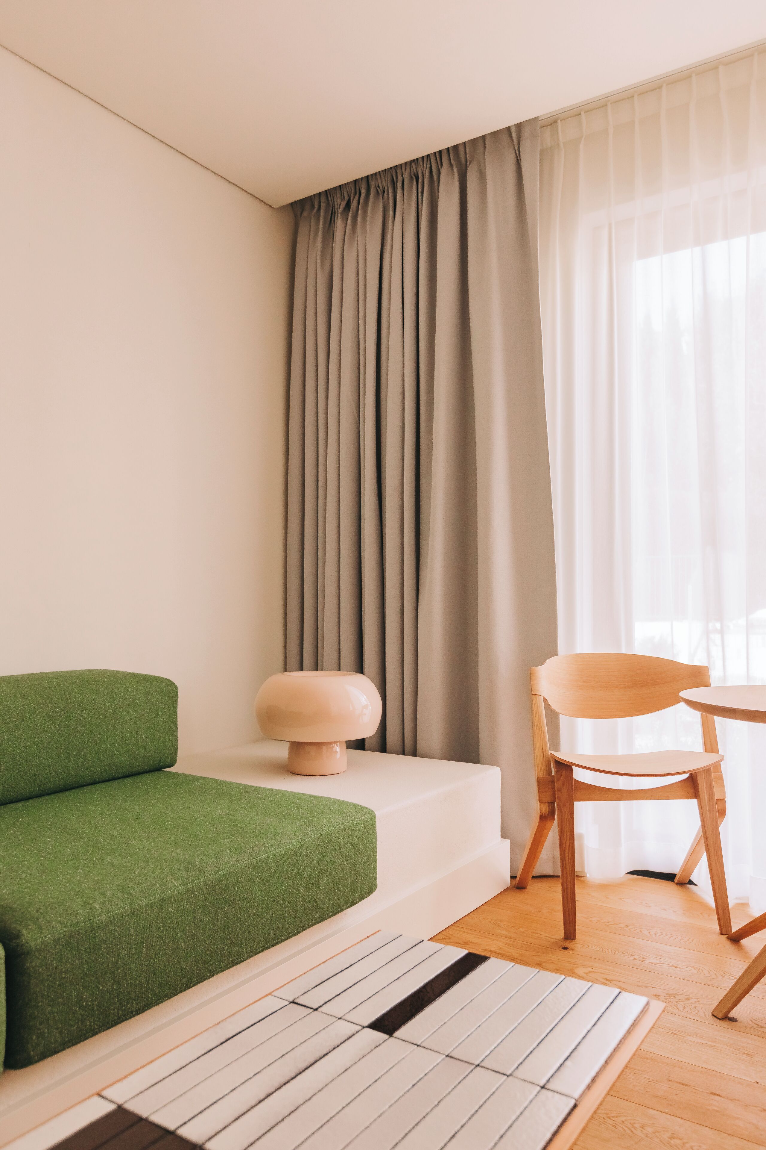 Ett modernt vardagsrum med en grön soffa, en trästol, ett litet bord och ett stort fönster med gardiner.