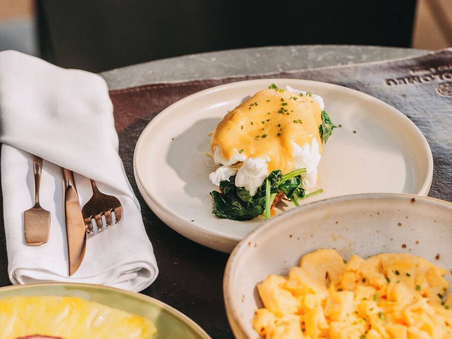 A table with a plate of scrambled eggs, a plate of fruit, and a plate of spinach and egg.