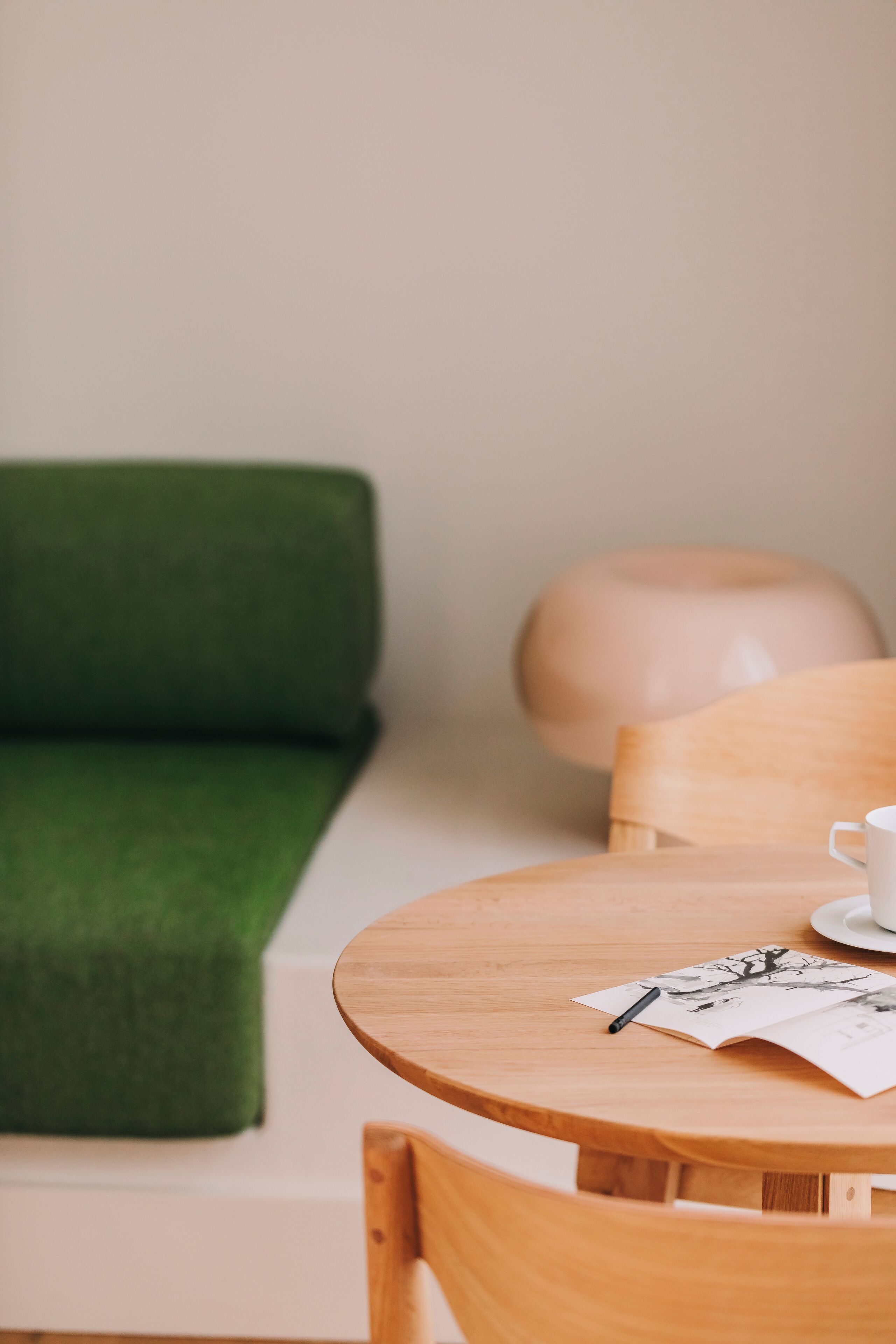 Une table ronde en bois, sur laquelle se trouvent une tasse et une soucoupe blanches, un stylo noir et un magazine ouvert.