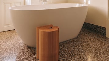 A modern bathroom with a freestanding bathtub, a wooden stool, and a speckled floor.