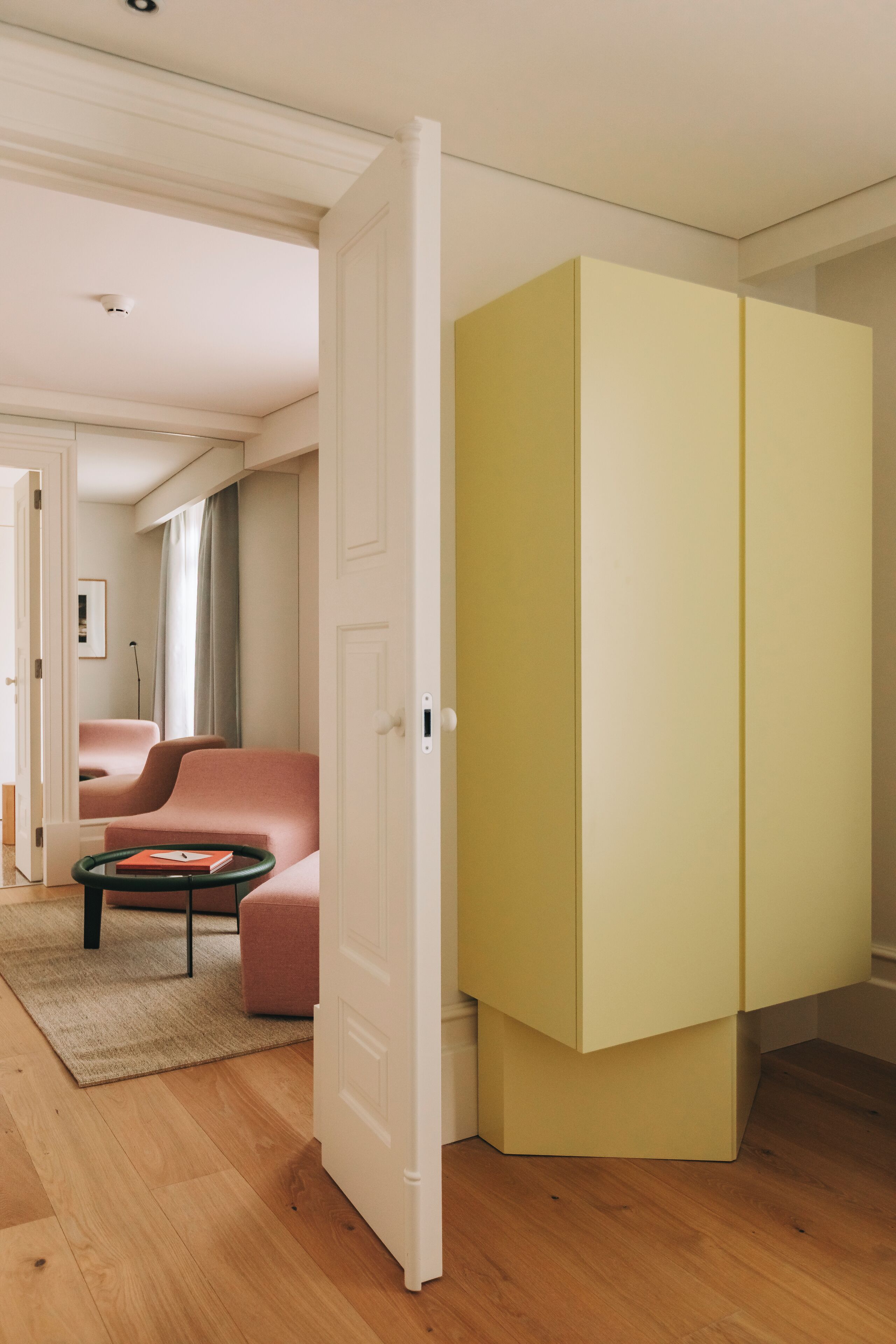 Una sala de estar moderna con piso de madera, un sofá rosa, una mesa de centro verde y un armario amarillo.