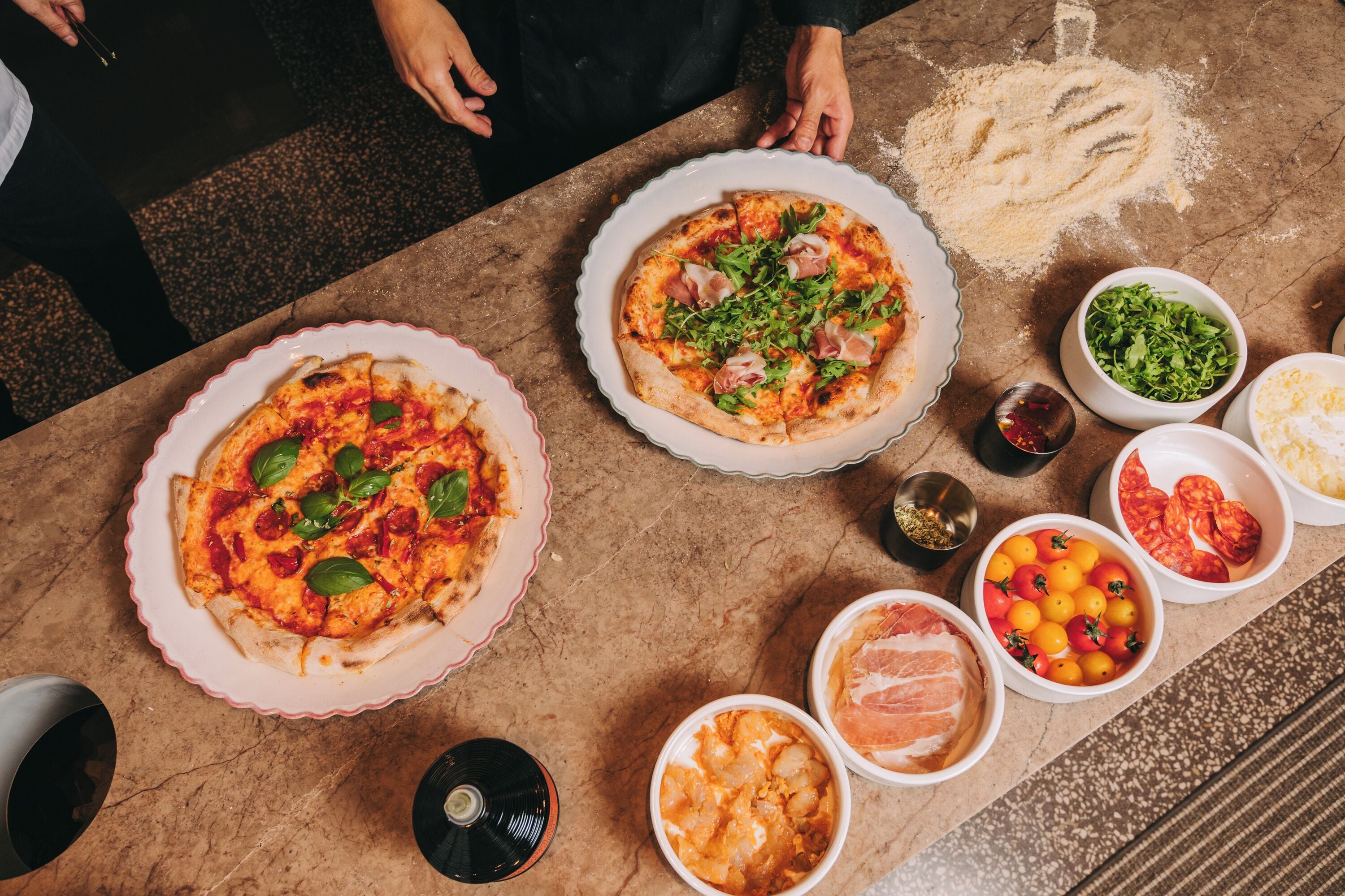 Una mesa con dos pizzas, diferentes condimentos y un CD.