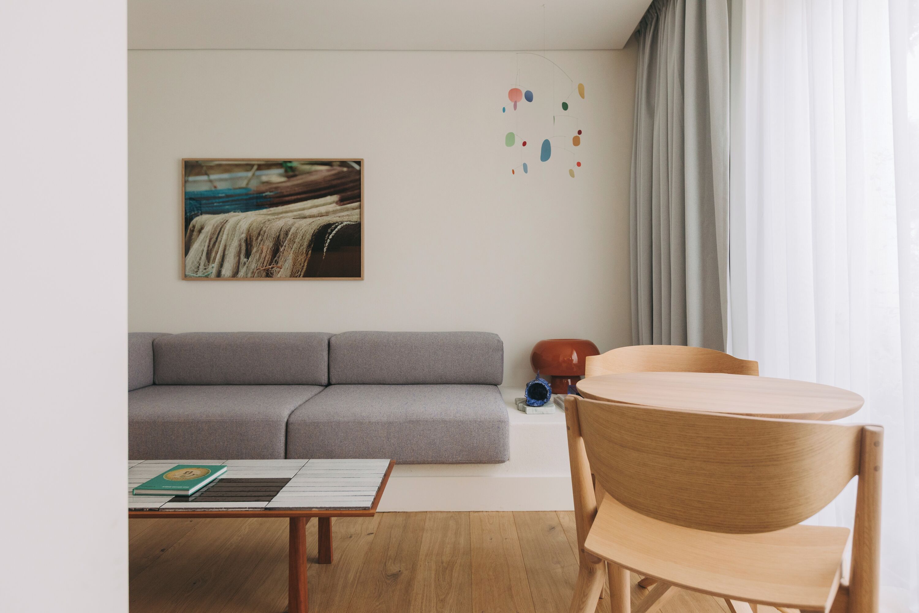 Un salon moderne avec un canapé gris, une table basse en bois et une table ronde en bois, accompagnée de chaises.