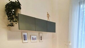 Een moderne woonkamer met een bank, een klein krukje, een vloerlamp en een wandplank met foto's en een klein beeldje.