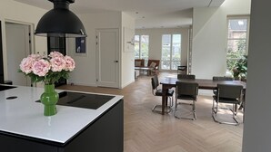A modern kitchen with a central island, a dining area with a table and chairs, and a view of the outdoors through large windows.