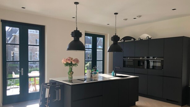A modern kitchen with a central island, black cabinets, and pendant lighting.