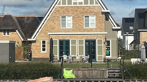 A two-story house with a gabled roof, a front porch with outdoor seating, and a small boat in the foreground.