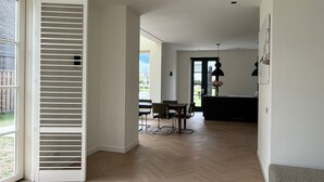 A spacious living area with a dining table and chairs, a kitchen island with a pendant light, and a large sliding door leading to a balcony.