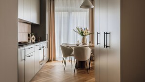 A modern kitchen with white cabinets, a dining area with a table and chairs, and a large window with sheer curtains. - Electra Apartments by StayLab (Kraków)