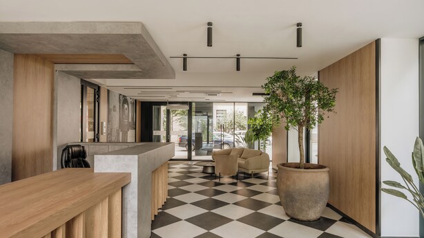 A modern reception area with a checkered floor, a wooden reception desk, a large potted plant, and a seating area with a sofa and armchairs. - Electra Apartments by StayLab (Kraków)
