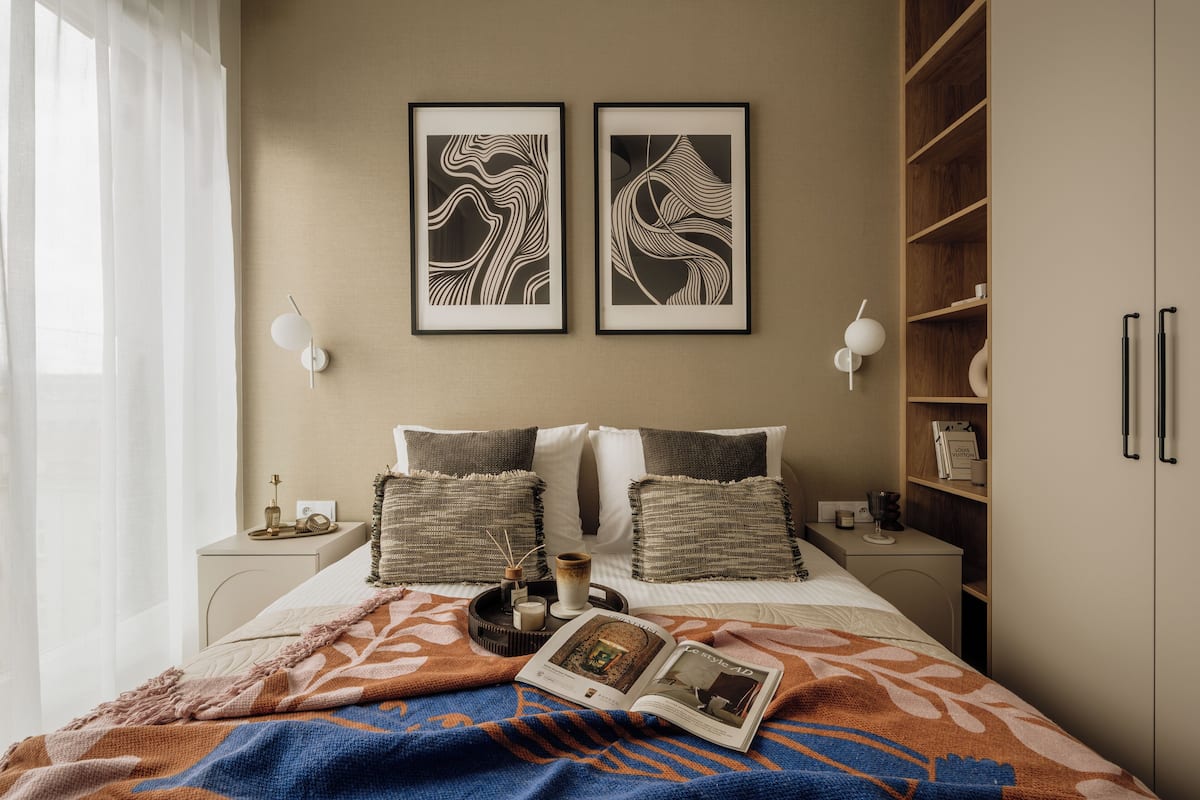 A neatly arranged bedroom with a bed, bedside tables, a bookshelf, and two framed artworks on the wall.