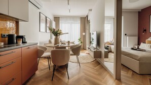 A modern living room with a sofa, a coffee table, and a TV. There is a dining area with a table and chairs, and a kitchen area with cabinets and a coffee machine. - Electra Apartments by StayLab (Kraków)