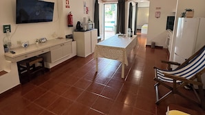 A spacious living area with a kitchen, a dining table, and a TV mounted on the wall.