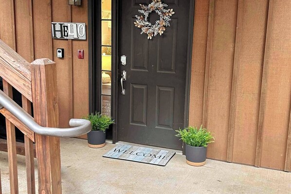 A wooden door with a 'WELCOME' mat and a 'HELLO' sign, two potted plants, and a metal handrail. - Lake Keowee Getaway with Dock Access, Pool & Mountain Views (Six Mile)