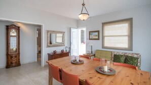 Un comedor con mesa de madera, sillas, un reloj, un espejo y una ventana con persianas.