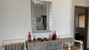 Een kamer met een witte console tafel, twee witte gestoffeerde stoelen, een spiegel met een sierlijk frame en een houten vloer.