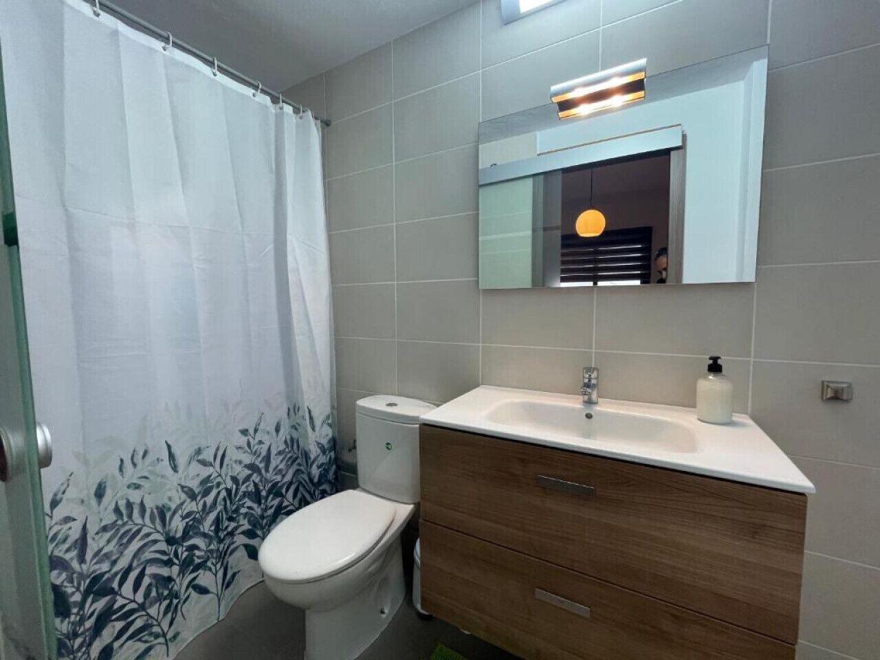 A bathroom with a toilet, a sink, a mirror, and a shower curtain.