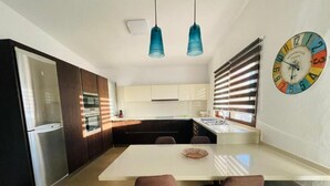 Een moderne keuken met een wit eiland, donkere kastjes, roestvrijstalen apparatuur en een kleurrijke klok aan de muur.