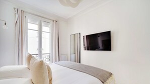 A bedroom with a large bed, a bedside table, a mirror, and a TV mounted on the wall. - Beautiful Apartment - 2bd/4p - Arc de Triomphe (Paris)