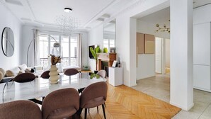 A modern dining area with a large table, brown chairs, and a chandelier. There is a fireplace with a mantel and a TV on the wall. - Beautiful Apartment - 2bd/4p - Arc de Triomphe (Paris)
