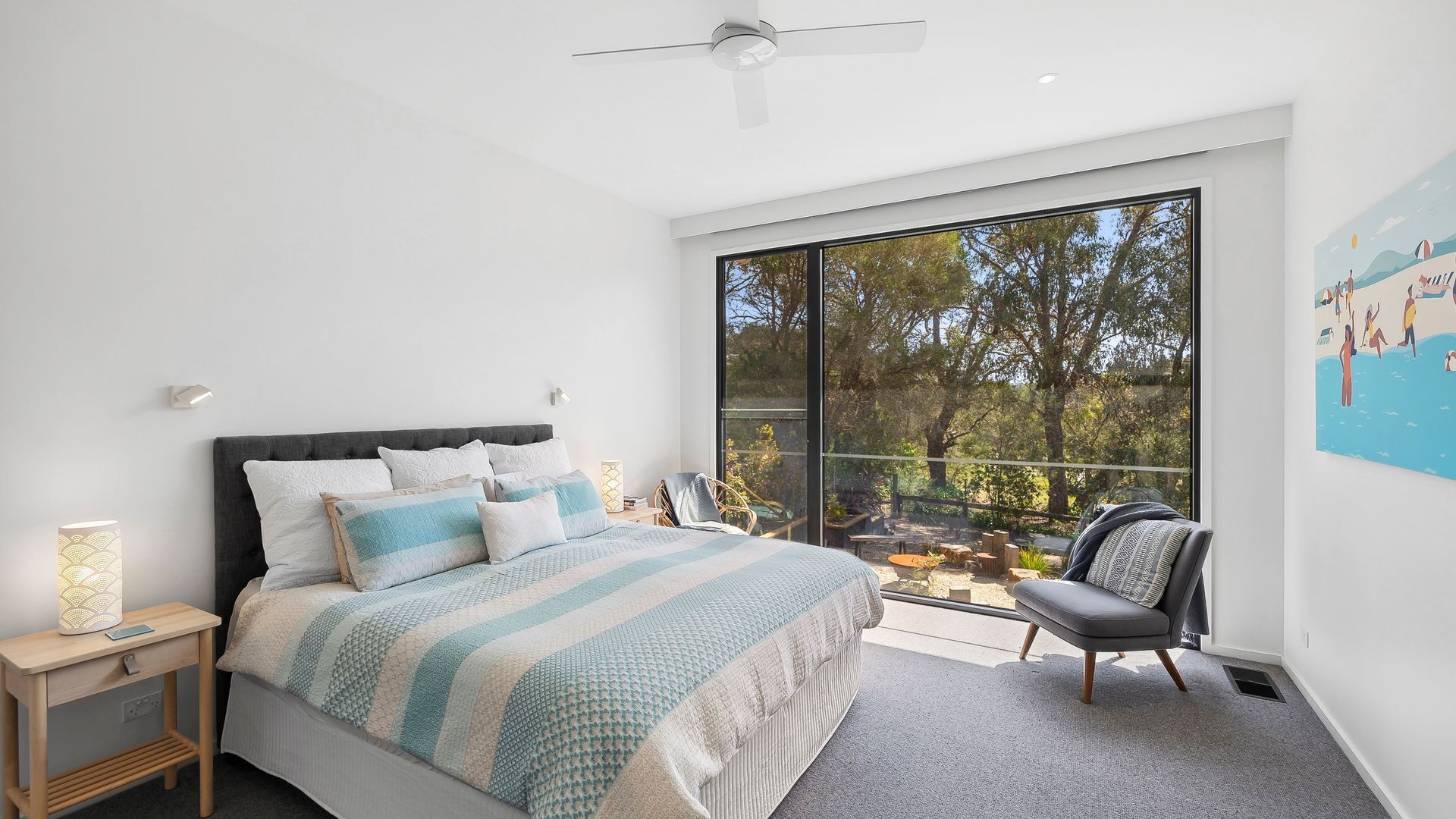 A modern bedroom with a large bed, a view of the outdoors, and a ceiling fan.