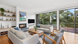 A modern living room with a fireplace, comfortable seating, a flat-screen TV, and a large window overlooking greenery. - Anglesea Summer Escape (Anglesea)
