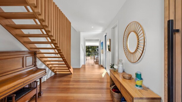 A modern interior with a wooden staircase, a piano, a console table with decorative items, and a large mirror. - Anglesea Summer Escape (Anglesea)