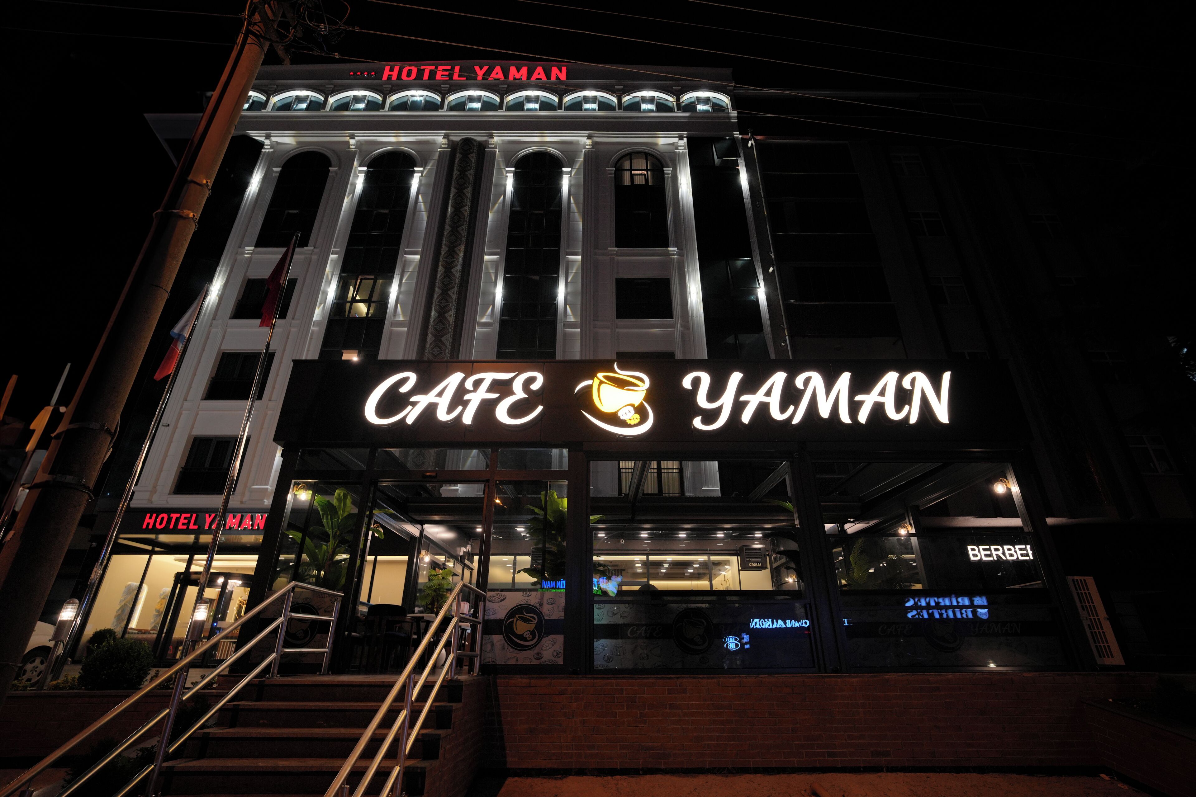 Un edificio con un llamativo letrero que dice 'Café Yaman', una escalera que conduce a la entrada y un letrero de 'Hotel Yaman' en la parte superior.