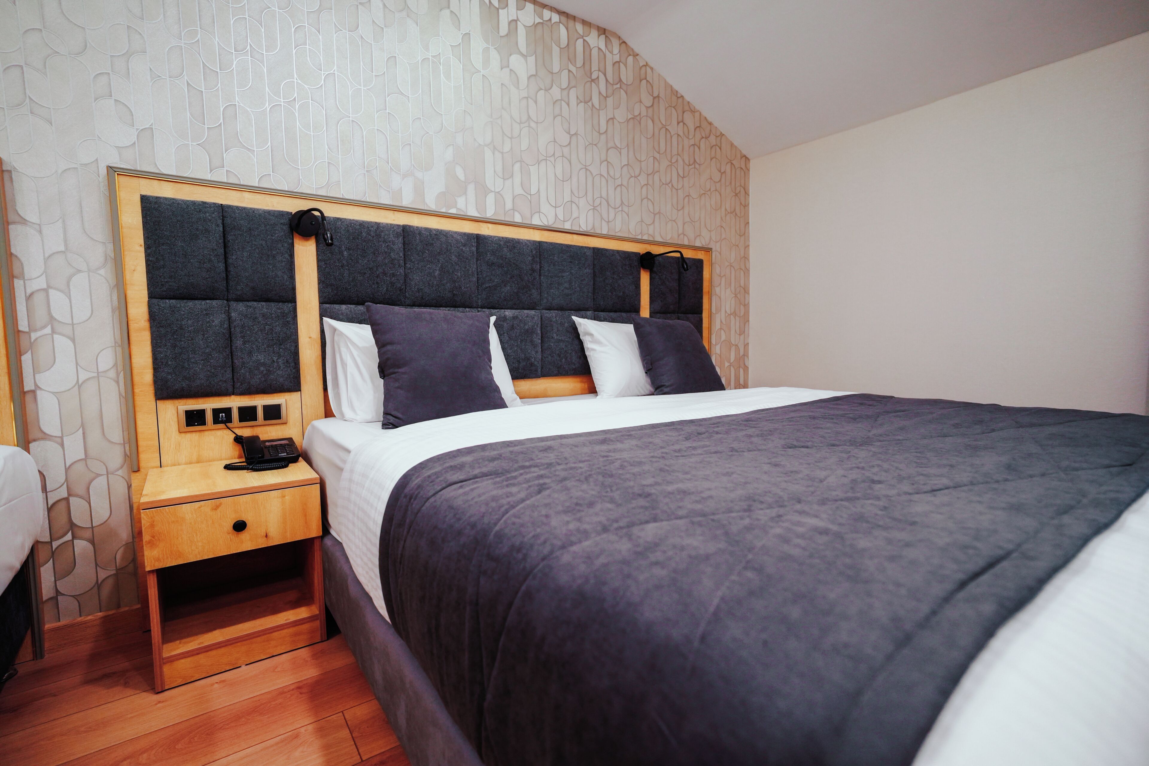 A modern bedroom with a large bed, a wooden nightstand, and a patterned wall.