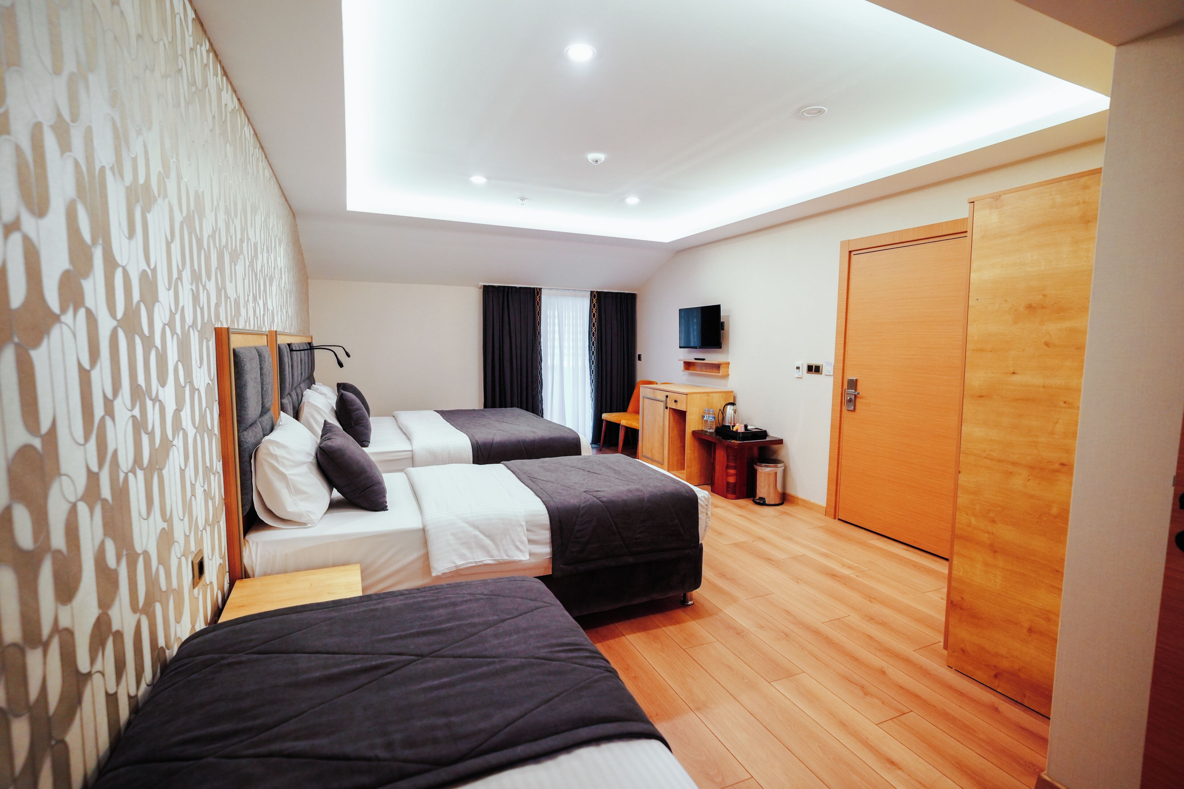 A modern hotel room with two beds, a desk, a TV, and a wooden wardrobe.