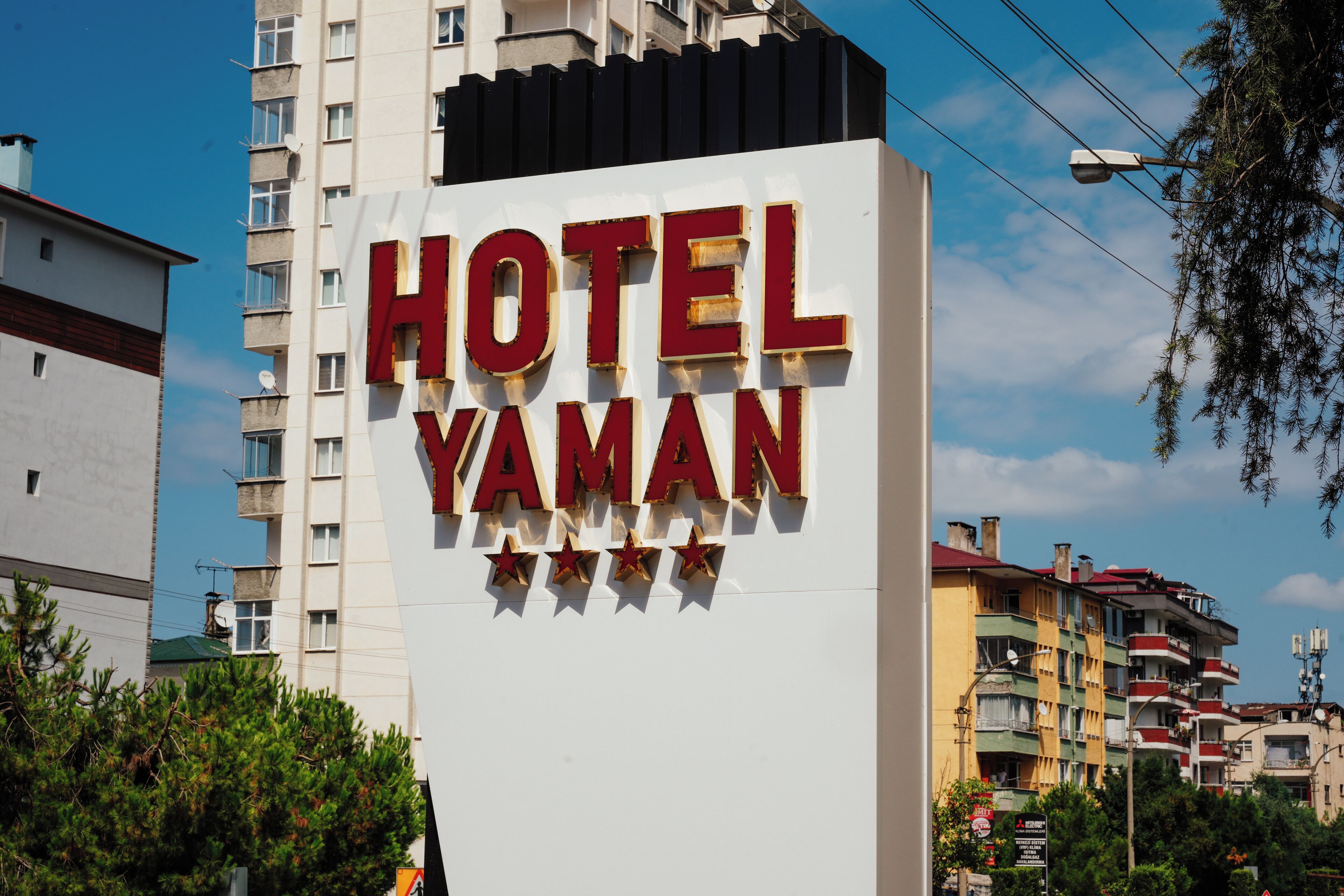 A sign for Hotel Yaman with a modern design, located in an urban area with surrounding buildings.
