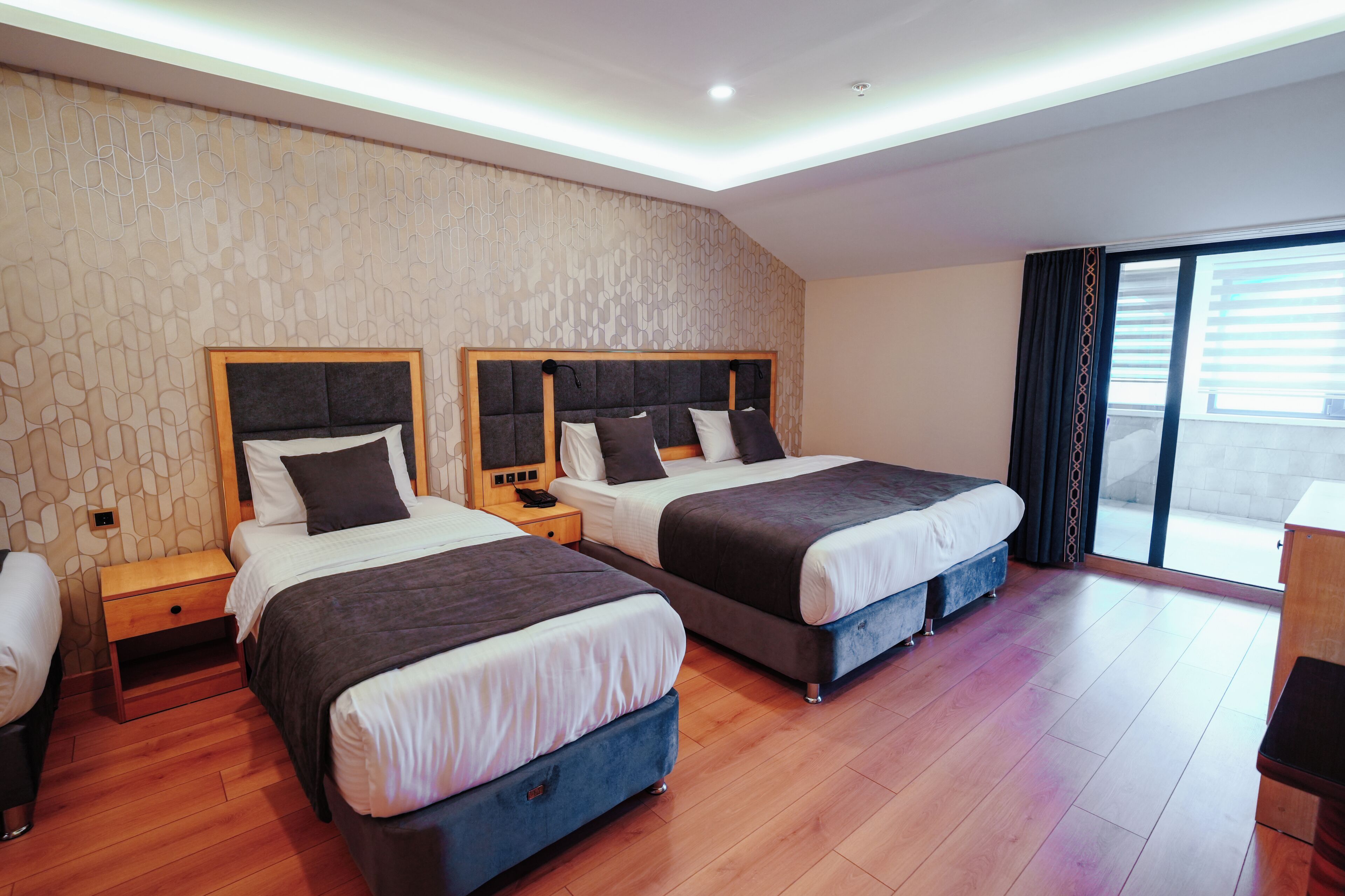 A hotel room with two beds, wooden floors, a patterned wall, and a large sliding glass door to the balcony.